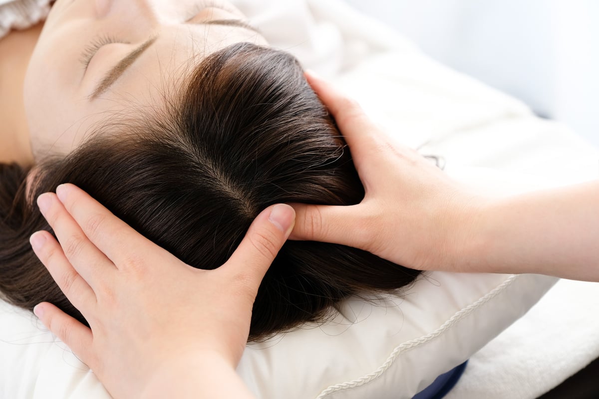 Woman receiving a scalp massage and the practitioner's hand